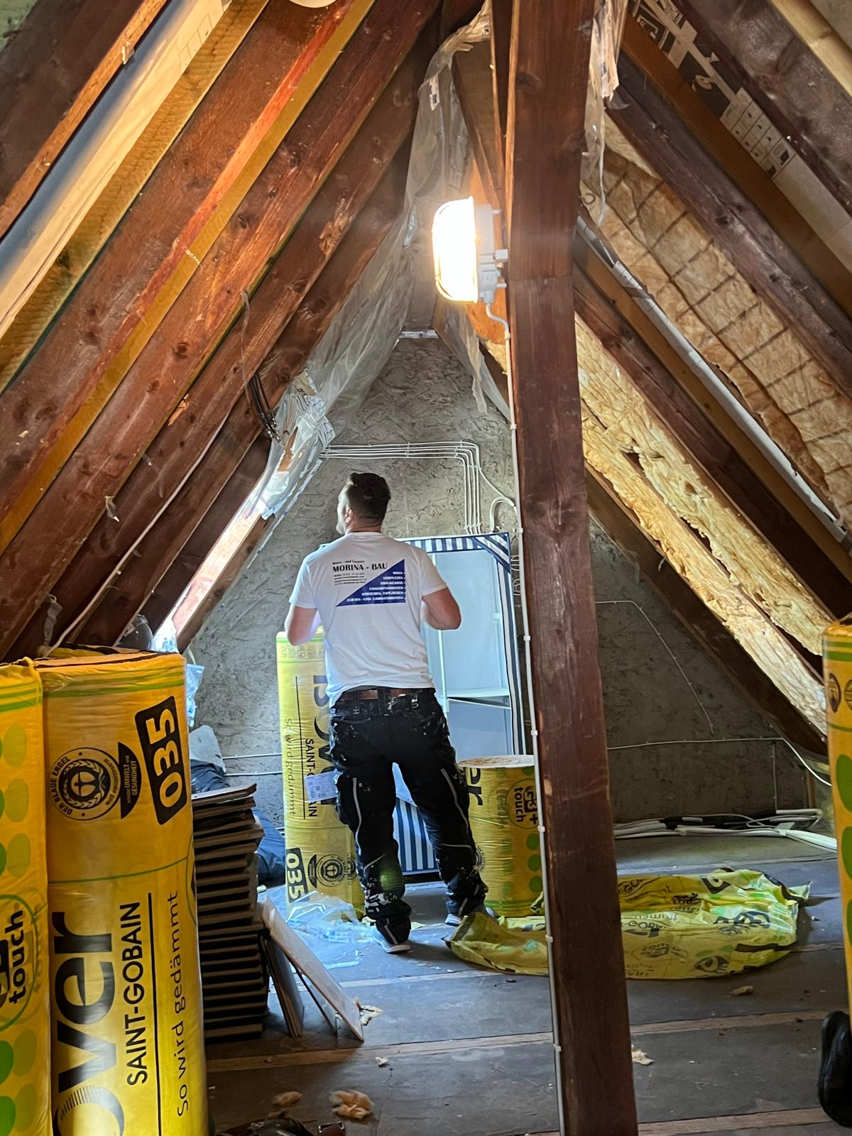 Dachboden mit Dämmrollen und Mitarbeiter beim Einbau
