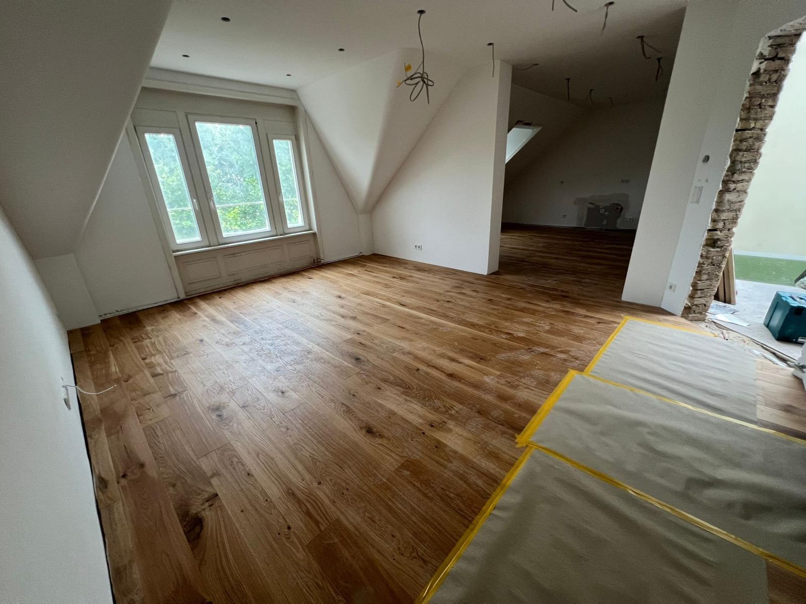 Großer Raum mit verlegtem Eichenboden, hängenden Kabeln, Werkzeugkoffer und rohem Ziegeldurchbruch
