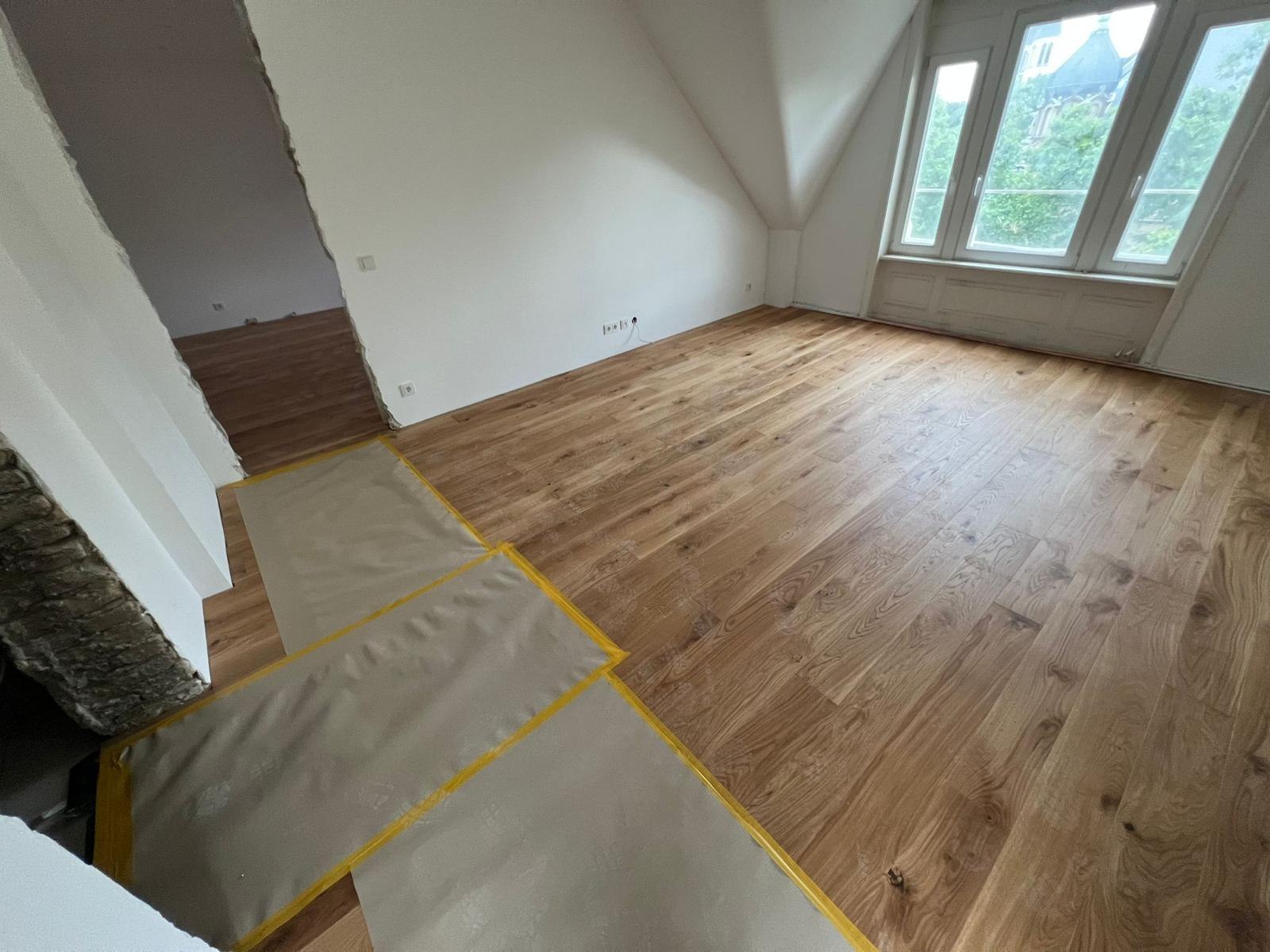 Zimmer mit verlegtem Eichenboden, Treppenabgang mit Malervlies und Klebeband abgedeckt