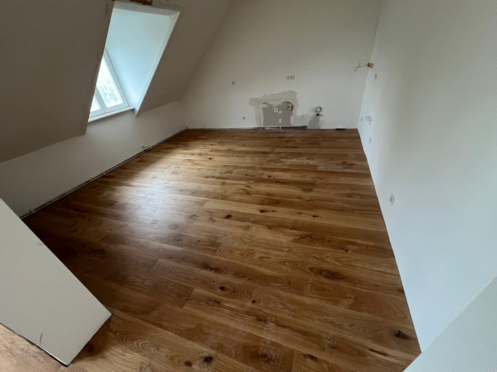 Dachzimmer mit verlegtem Eichenboden, unverspachtelten Wandstellen und Kabeln aus der Wand