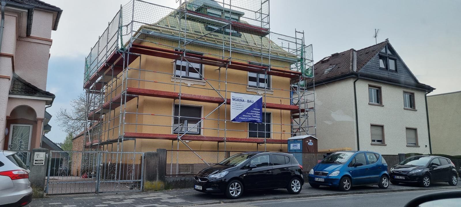 Eingerüstetes Wohnhaus im orangefarbenen Grundputz mit Bauschild von Morina-Bau