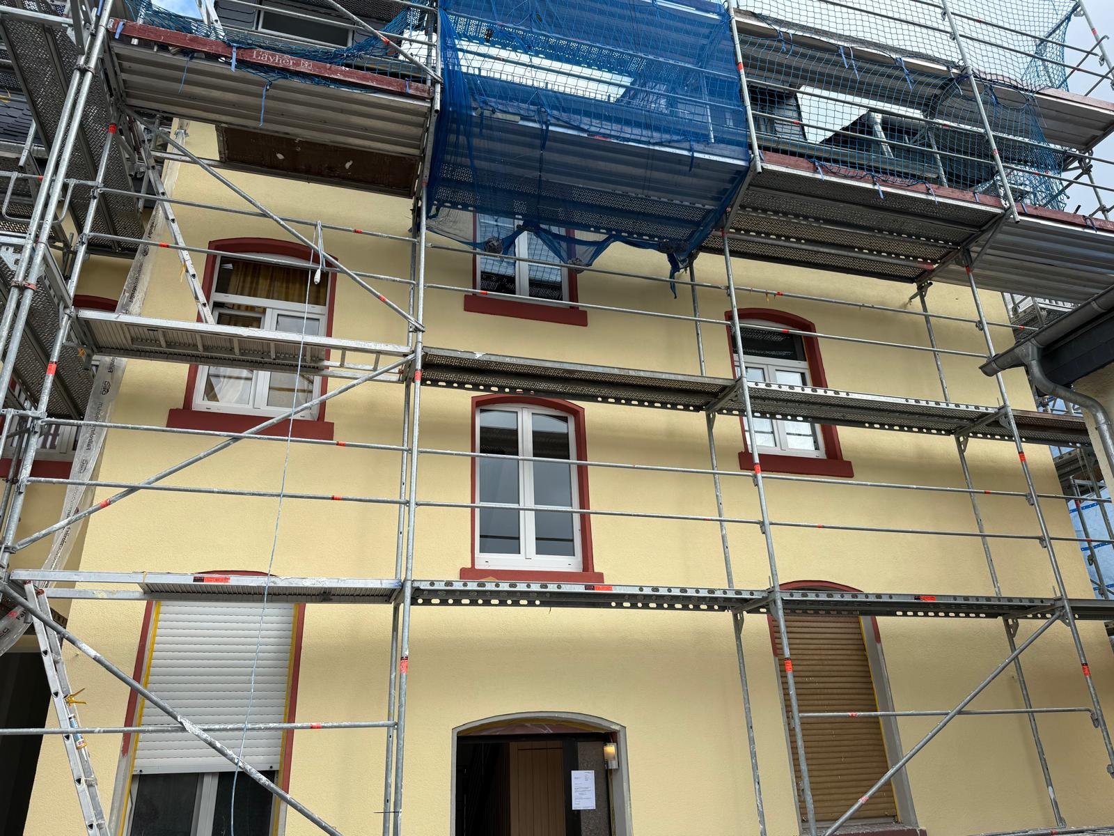 Altbaufassade in Creme mit rotbraun abgesetzten Fenstergewänden, noch im Gerüst