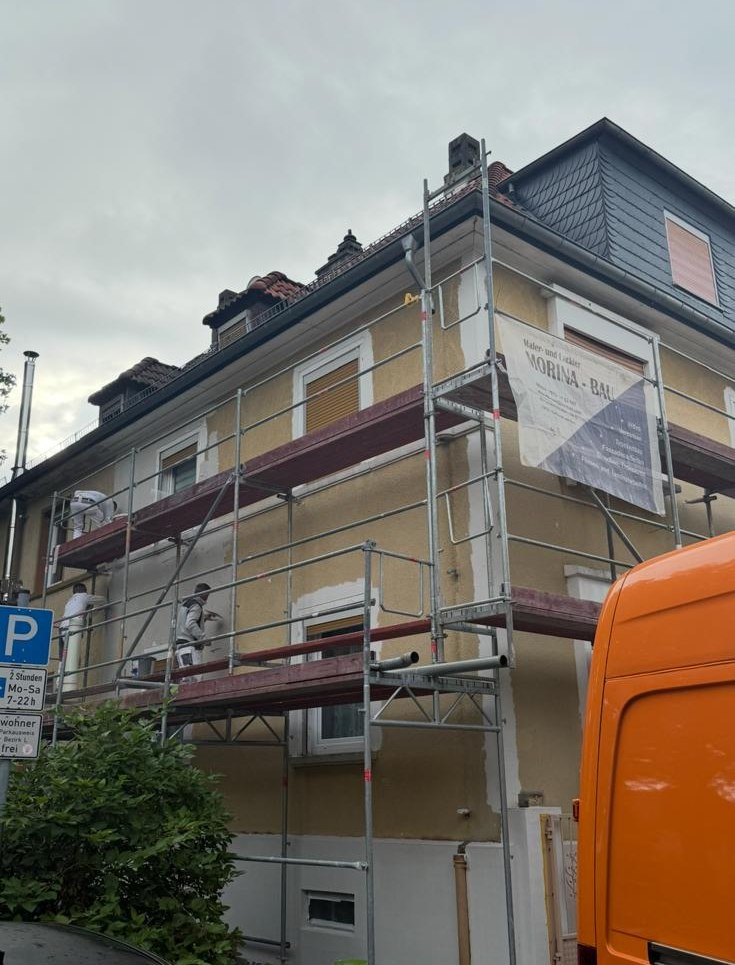 Altbaufassade im Gerüst mit abgeschlagenem gelbem Putz und Bauschild