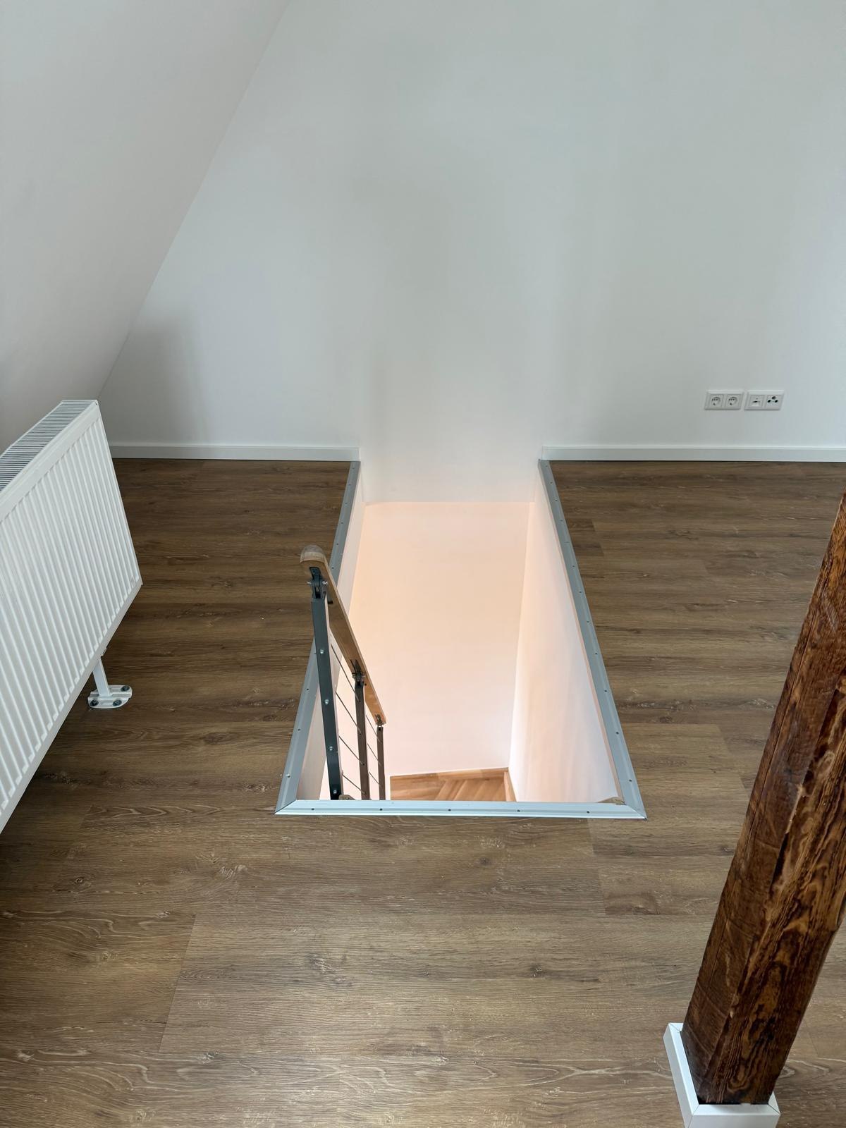 Dachwohnung mit dunklem Vinylboden, Treppenöffnung und freigelegtem Holzbalken