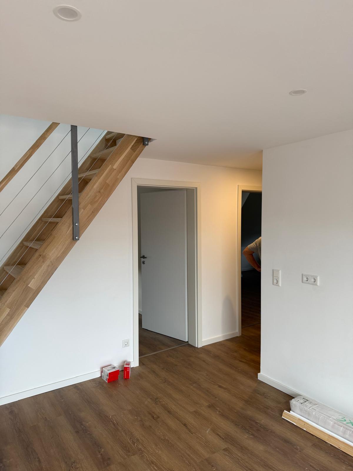 Wohnraum mit dunklem Vinylboden, offener Treppe und weißen Wänden