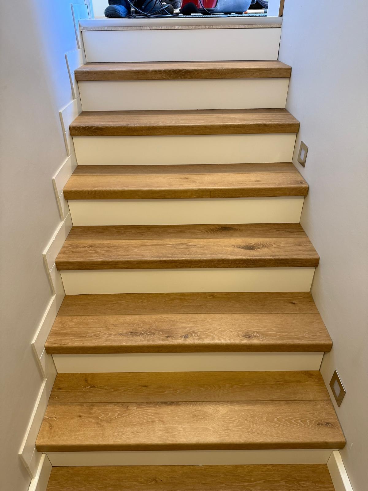 Treppe mit Eichenstufen, weißen Setzstufen und eingelassenen Wandleuchten