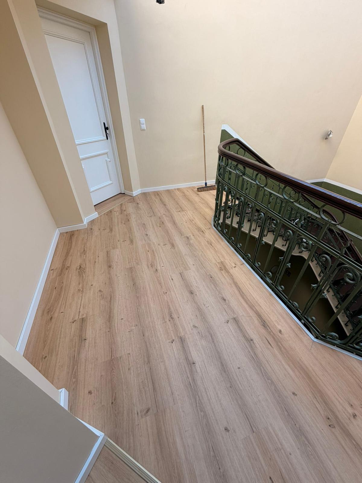 Altbau-Treppenhaus mit neuem hellem Vinylboden und grünem Gusseisengeländer