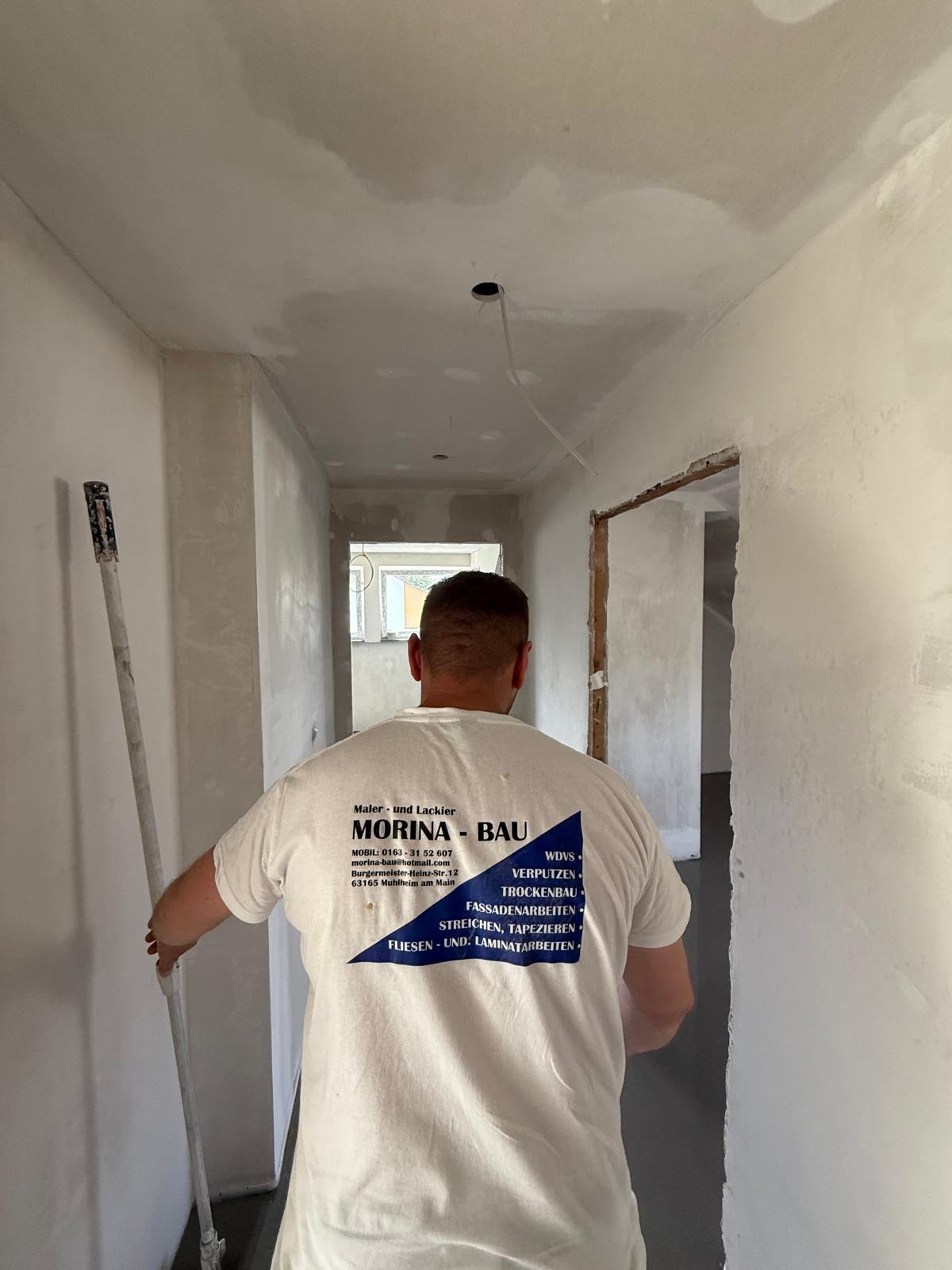 Mitarbeiter mit Spachtelstange im Flur, Decke bereits verspachtelt
