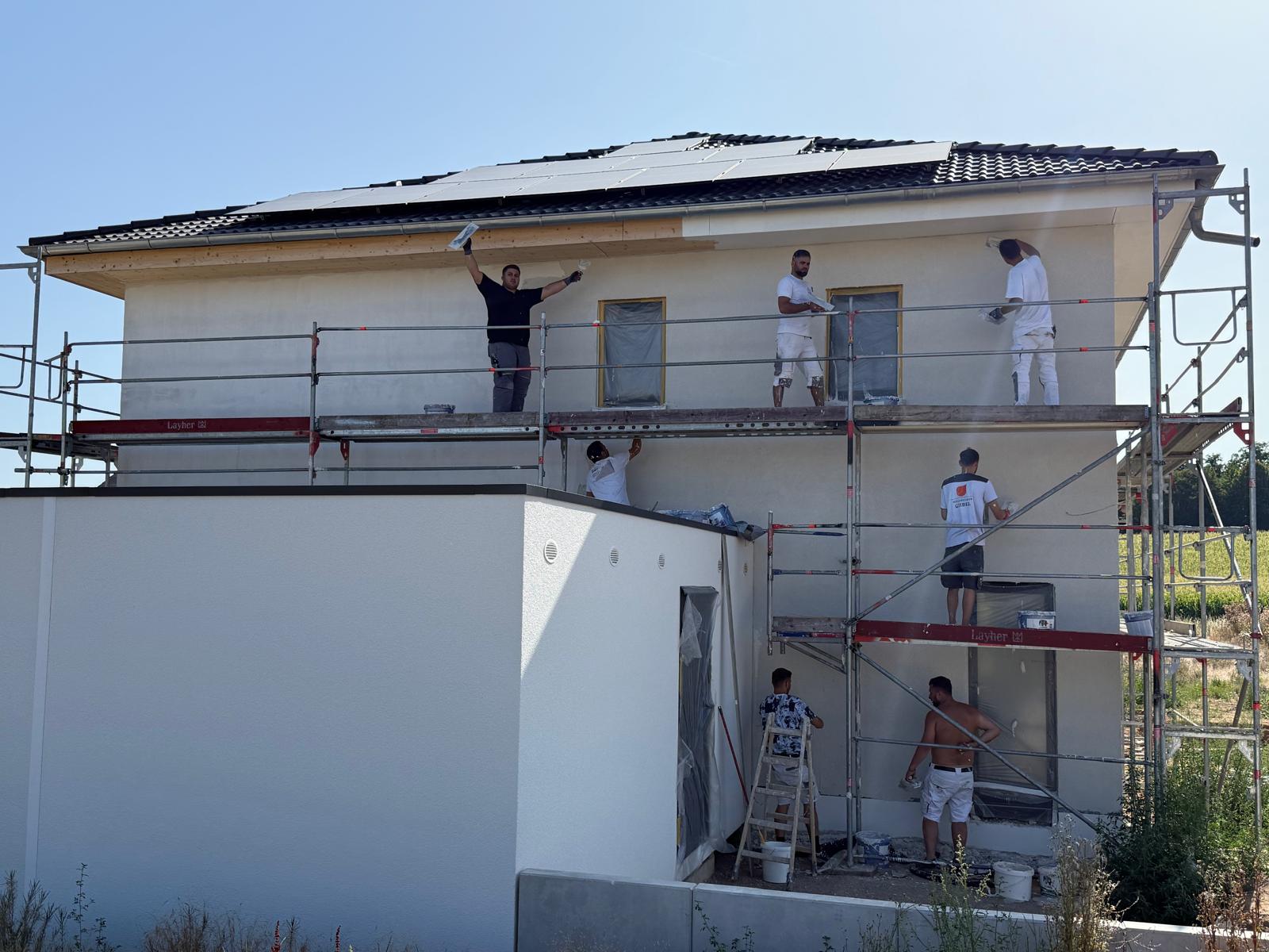 Mehrere Mitarbeiter von Morina-Bau verputzen eine Neubaufassade vom Gerüst aus